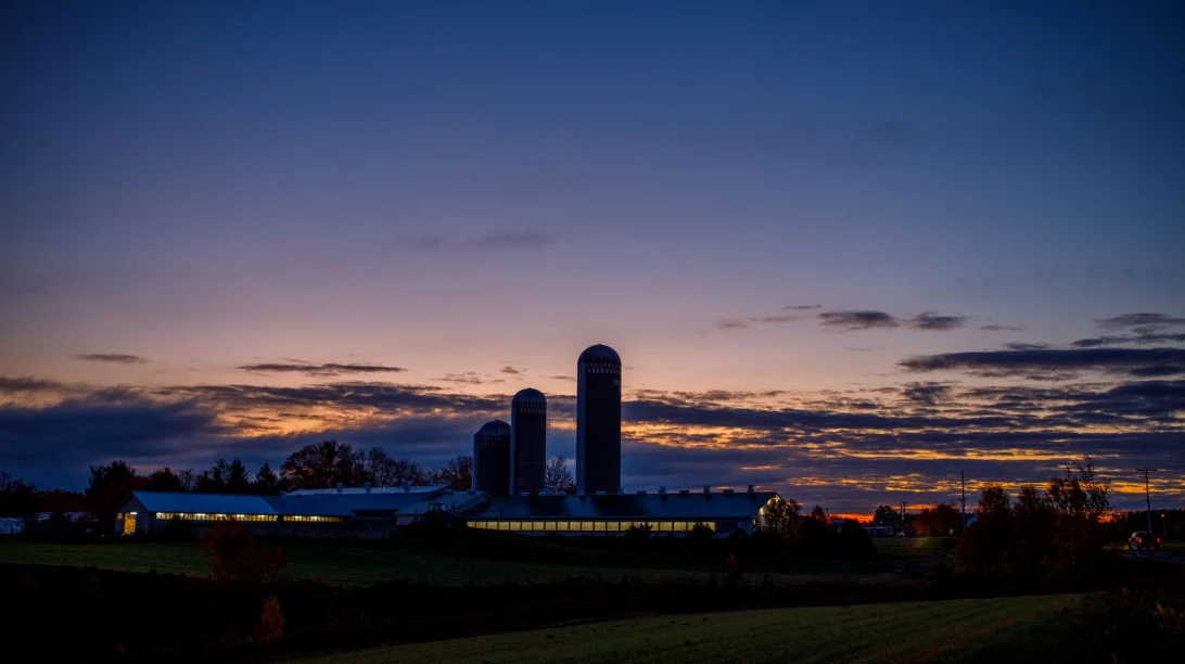 Vue de loin d'une ferme durant un coucher de soleil.