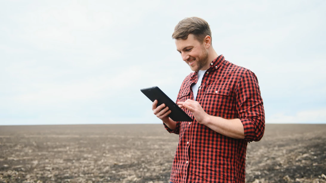 Homme tenant une tablette dans un champ au sol nu