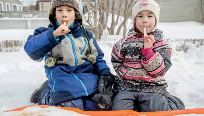 Deux enfants en train de manger de la tire d'érable à l'extérieur.