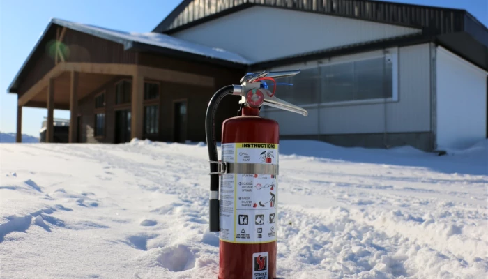 Un extincteur dans la neige devant une bâtisse agricole