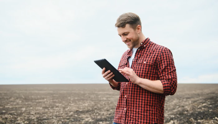 Homme tenant une tablette dans un champ au sol nu